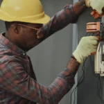 man in brown and white plaid dress shirt and yellow hard hat holding black and orange