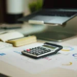 Calculator, laptop and printed charts on a desk, for working out what a Shopify store costs
