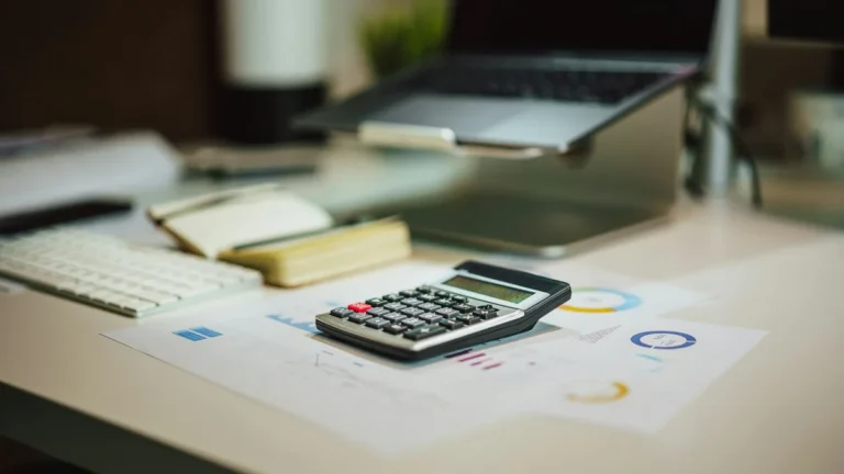 Calculator, laptop and printed charts on a desk, for working out what a Shopify store costs