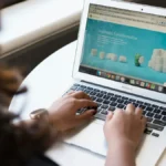Hands typing on a laptop that shows an online store page, illustrating Shopify theme customization